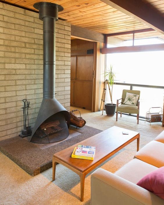 a relaxed mid-century modern living room with a black Malm fireplace, neutral and pastel seating furniture, a wooden coffee table and potted bamboo