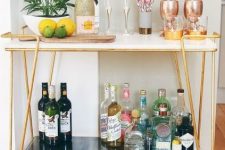 a small and chic gold home bar cart with open storage spaces and potted greenery is very stylish