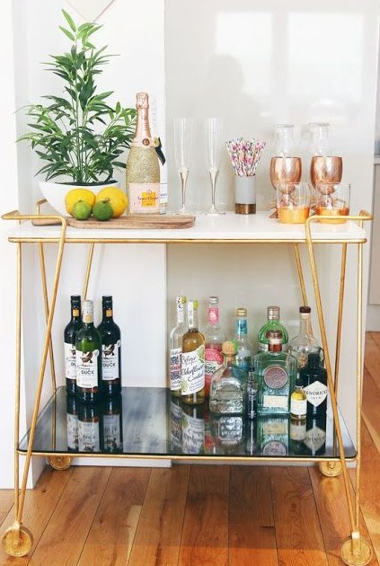 a small and chic gold home bar cart with open storage spaces and potted greenery is very stylish