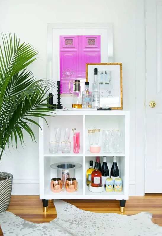 a small and cool home bar made of an IKEA piece, with a bright artwork, copper barware and gold edge glasses