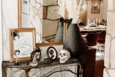a stylish Halloween console with pillar candles, black cheesecloth, signs and artworks, skulls and blackbirds, a black vase with pampas grass