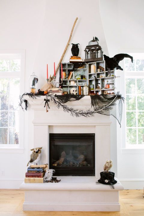 a unique Halloween mantel with black cheesecloth, blackbirds and owls, orange candles, books, skulls and lanterns is amazing