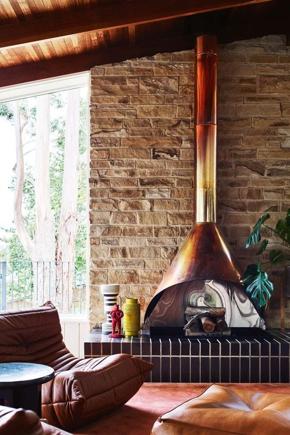 a warm-colored mid-century modern living room with a brick accent wall, a bright Malm fireplace, navy tiles, an amber leather chair and pouf