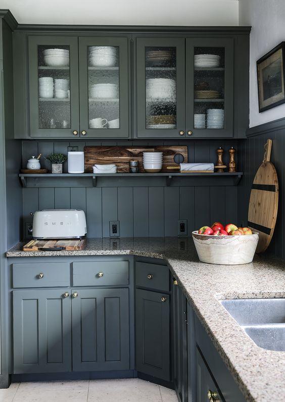 a welcoming cottage kitchen with grey cabinets and a matching planked backsplash, with stone countertops and wooden decor