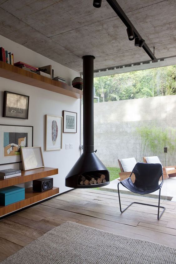 a welcoming mid-century modern living room with a black suspended Malm fireplace, a black leather chair, open shelves with books and art