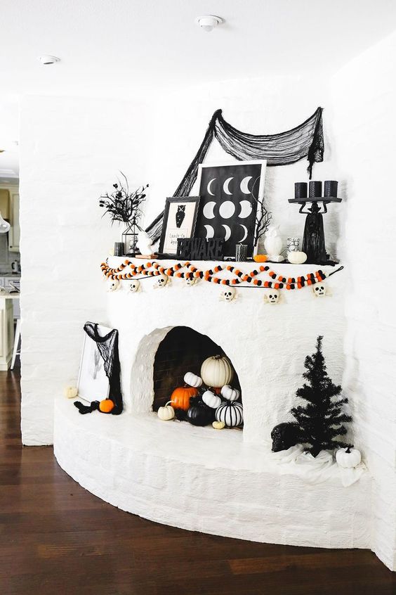 a white fireplace with colorful garlands with skulls, signs, black candles on a stand, black cheesecloth and branches and some pumpkins in the fireplace