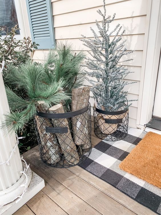 a wire basket with firewood and fir branches and a basket with a flocked Christmas tree for a slight rustic feel in the porch