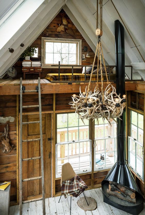 a woodland cabin featuring a black Malm fireplace, a leather chair and a loft bedroom upstairs looks unusual and cozy