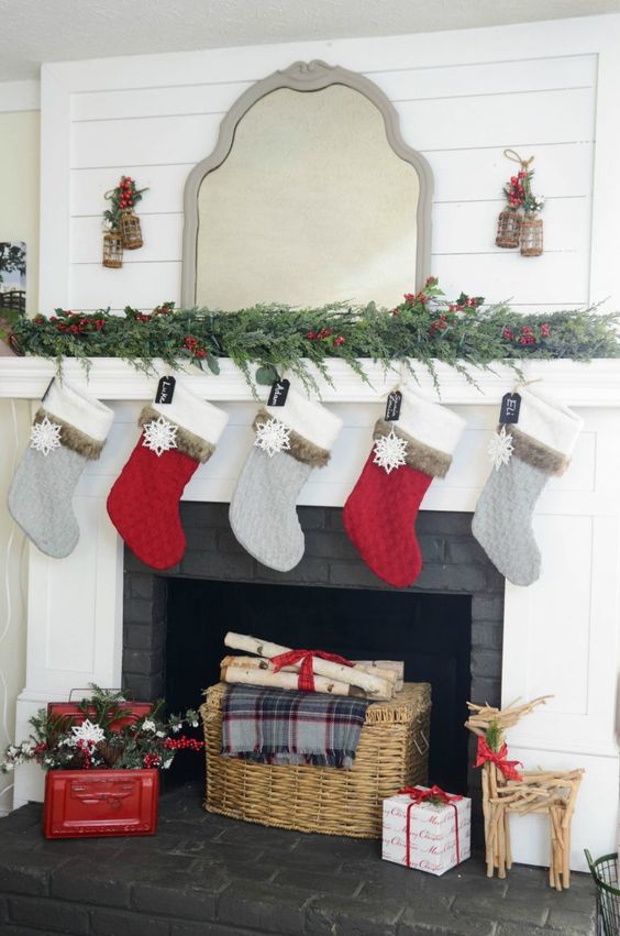 an evergreen garland with berries, red and grey stockings, a basket and firewood, a red chest with evergreens