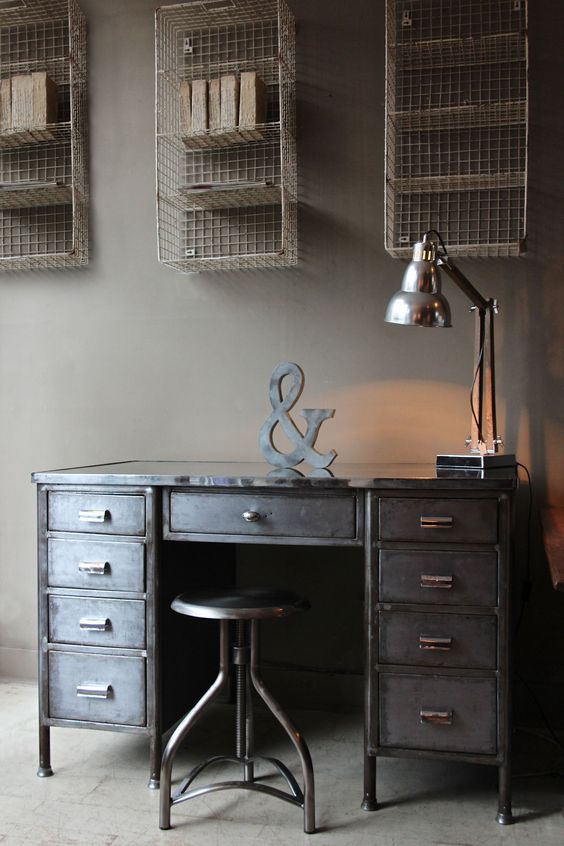 an industrial desk made of aged metal, with a matching stool and a chic table lamp plus open shelving units over the desk
