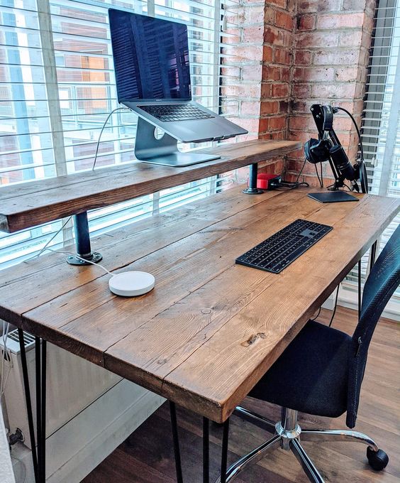 an industrial desk of wood, with an additional shelf to use it as a standing desk, metal hairping legs and a black chair