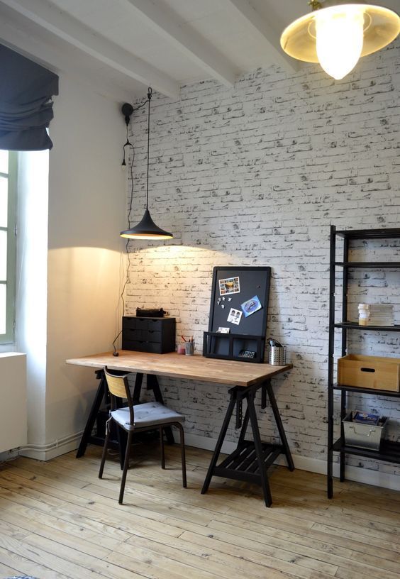 an industrial home office with white brick walls, a trestle desk of wood and metal, a pretty chair and pendant lamps