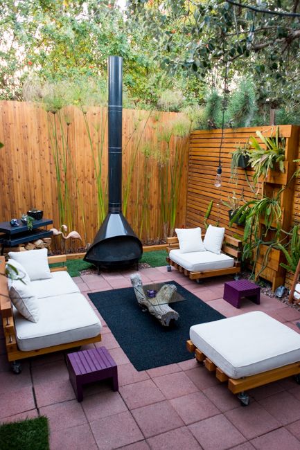 an outdoor space with white seating furniture, a black Malm fireplace, a black rug, purple stools and potted greenery