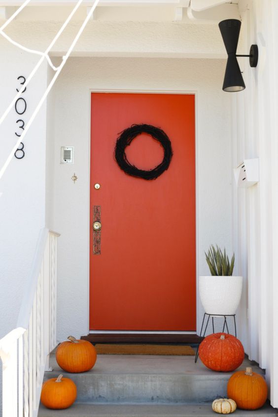 bright pumpkins and a black wreath on the orange door are perfect to style your modern front porch for Halloween
