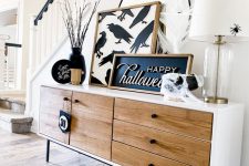 chic Halloween console table styling with a sign and an artwork, black plates and branches, a black cauldron and a mirror with a spider
