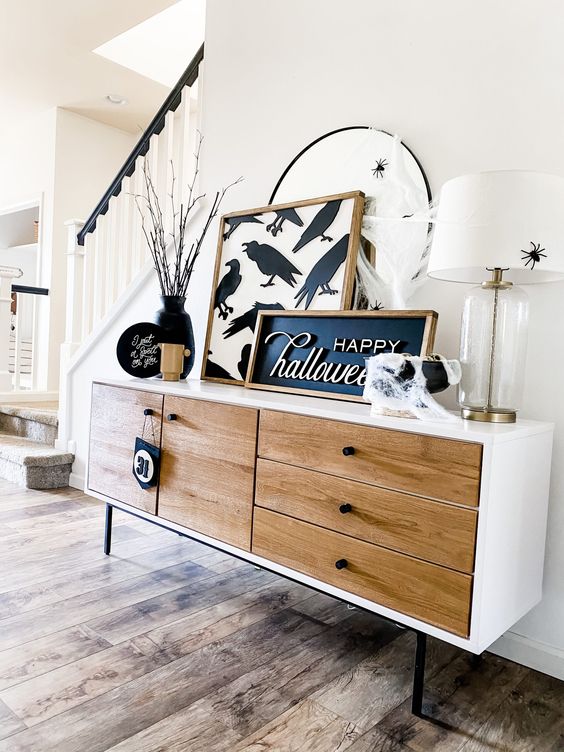 chic Halloween console table styling with a sign and an artwork, black plates and branches, a black cauldron and a mirror with a spider
