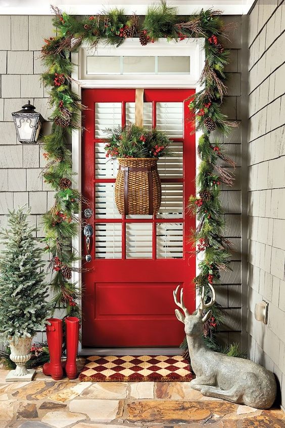 cozy rustic Christmas front door styling with an evergreen garland with berries and pinecones, a snowy mini tree and red boots