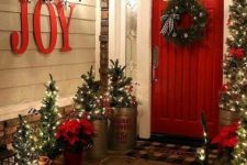 lots of mini Christmas trees with lights, JOY letters, a wreath and red touches for a lovely rustic front porch