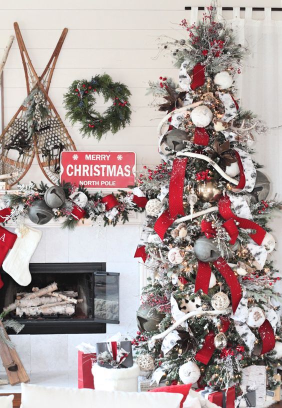 lovely grey, red and white Christmas decor with a tree with oversized bells, ribbons and lights, a matching garland on the mantel and vintage skis