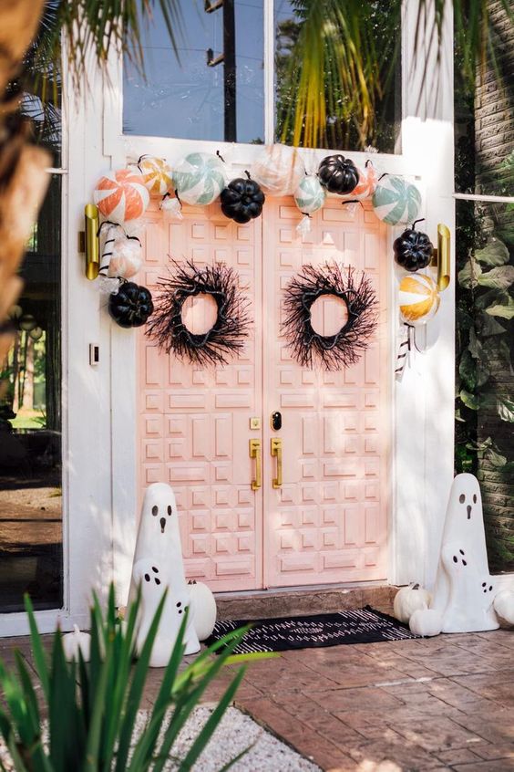 pretty Halloween front doors with black branch and snake wreaths, pastel and black pumpkins over them and mini ghosts on the floor