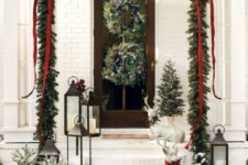 rustic Christmas front door decor with evergreen wreaths with pinecones, an evergreen garland with red ribbons and mini snowy trees