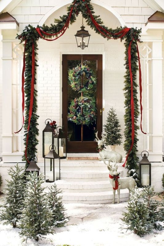 rustic Christmas front door decor with evergreen wreaths with pinecones, an evergreen garland with red ribbons and mini snowy trees