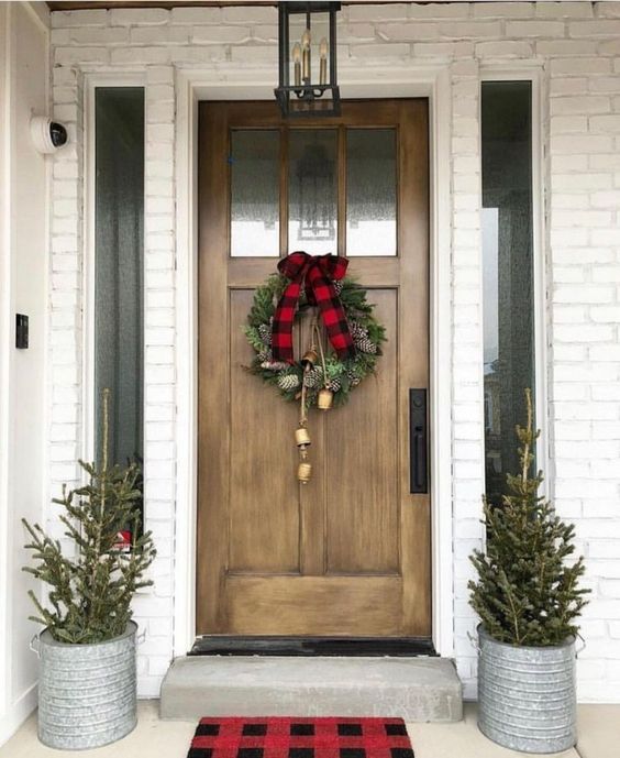 simple Christmas styling with mini trees in buckets, an evergreen wreath with bells and a plaid bow on top