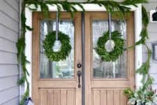 simple natural Christmas front door styling with an evergreen garland and wreaths, candle lanterns and a pale greenery arrangement