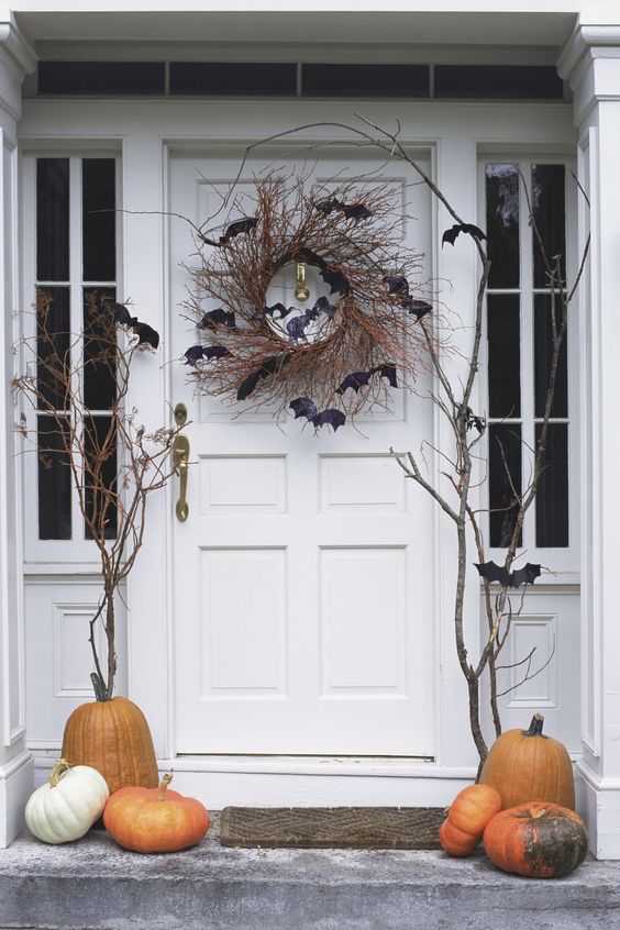 simple rustic Halloween front porch styling with pumpkins, branches, black bats and a twig wreath on the door