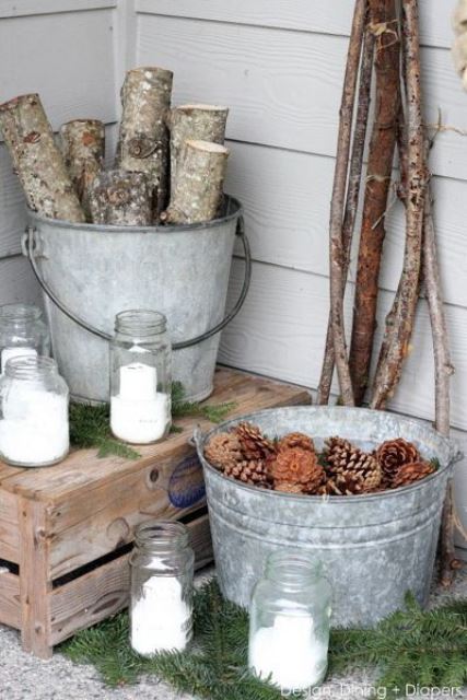 some branches, firewood in a bucket, a bucket with pinecones, candles in glass jars and fir branches for a cozy feel in the porch