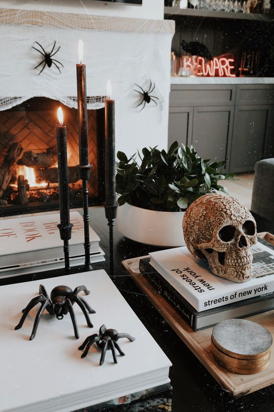 stylish Halloween decor with black candles in candleholders, black spiders, a beautiful ornated skull abd some spiders on the fireplace