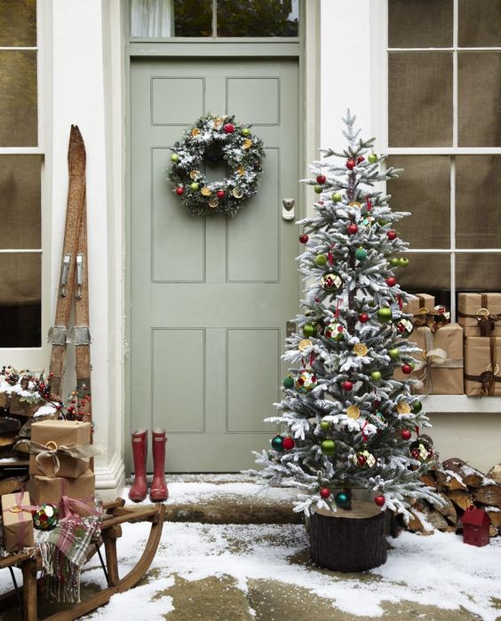 vintage-inspired Christmas front door decor with a cute wreaht with citrus slices and ornaments and a Christmas tree decorated with them, a sleigh with gift boxes and skis