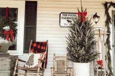 wooden rockers with a plaid blanket and a printed pillow, a Christmas tree in a bucket with a red bow, a vintage sleigh with a bow and a wreath