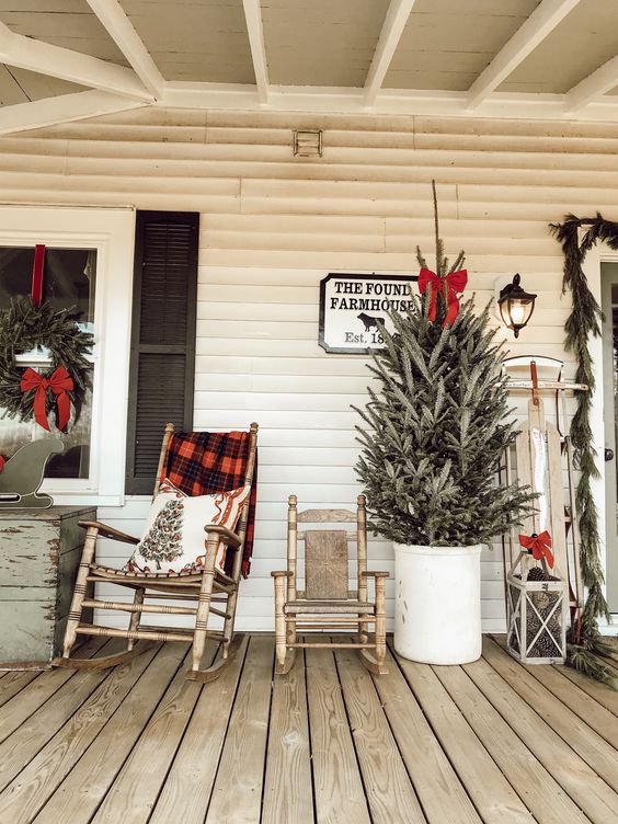 wooden rockers with a plaid blanket and a printed pillow, a Christmas tree in a bucket with a red bow, a vintage sleigh with a bow and a wreath