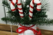 a Christmas centerpiece or just decoration of a white jar with fir branches, candy canes, berries and a red bow is a lovely idea