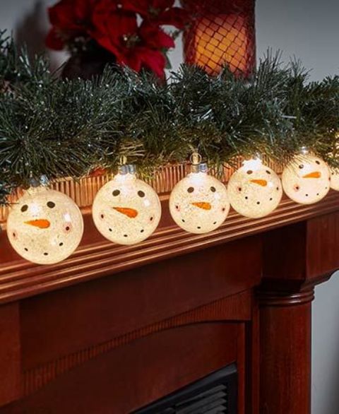 a Christmas mantel with an evergreen garland and a lit up snowman one is a creative decor idea with a slight retro feel