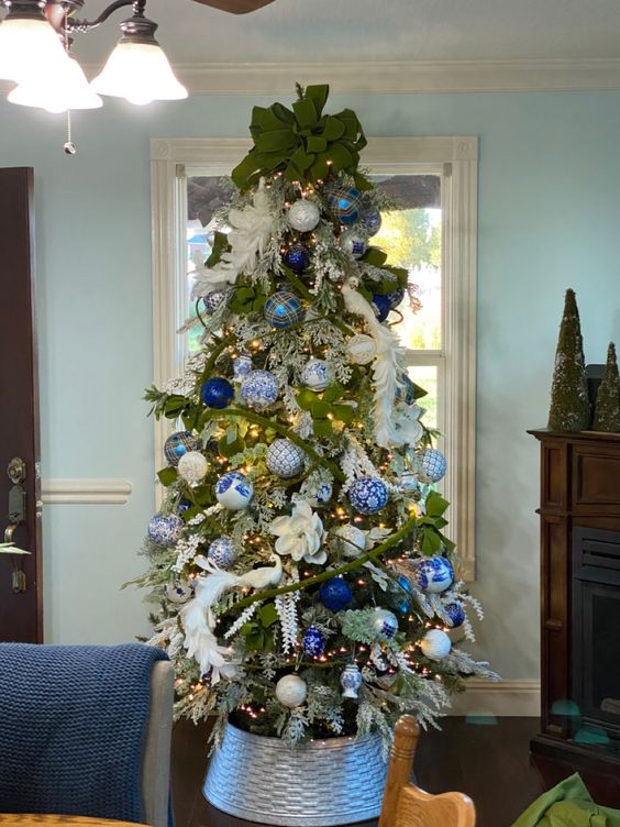 a beautiful Christmas tree with white feathers and fabric blooms, blue and white ornaments, a large green bow on top is amazing