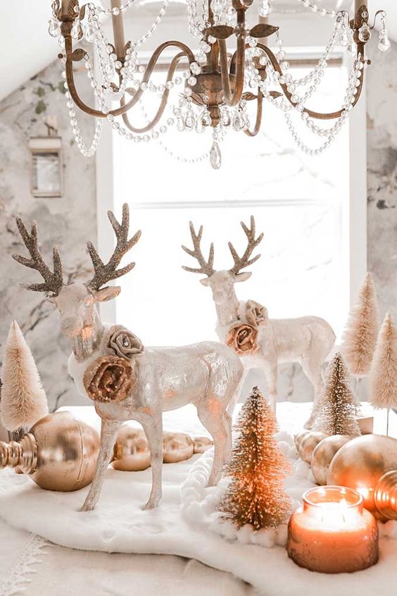 a beautiful glam Christmas tablescape with oversized gold ornaments, mini bottle brush Christmas trees, shiny deer with gold roses and a crystal chandelier