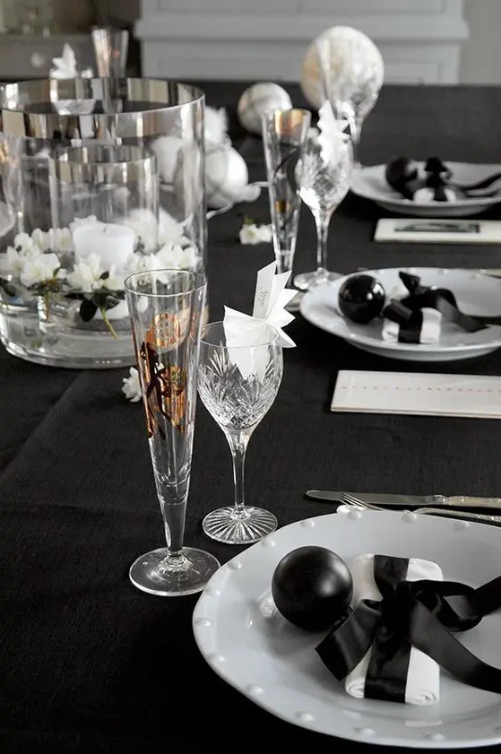 a black and white tablecape with floating flowers, a candle, black ornaments and white napkins