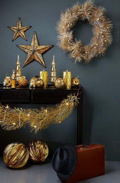 a black console table with oversized gold balls, gold patterned candles, a gold wreath and stars plus lights is amazing for the holidays