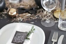 a black tablescape with black and metallic ornaments and table runner, chalkboard cards and white chargers