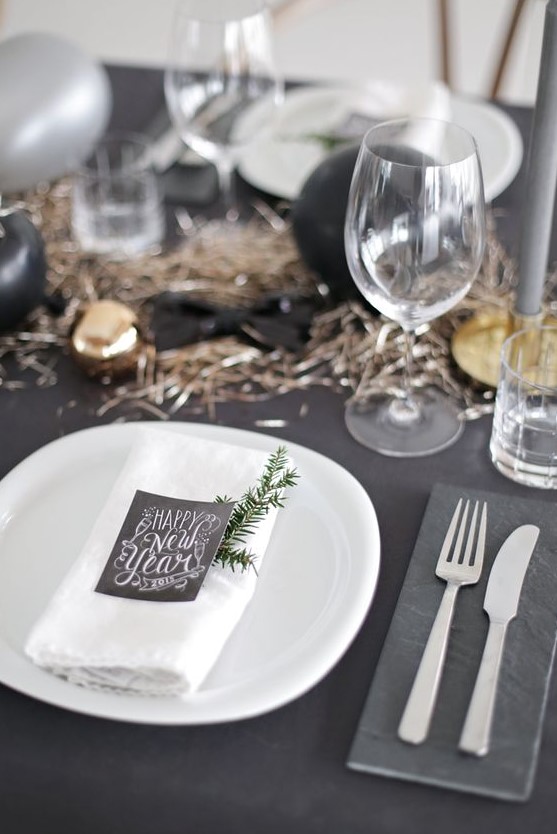 a black tablescape with black and metallic ornaments and table runner, chalkboard cards and white chargers