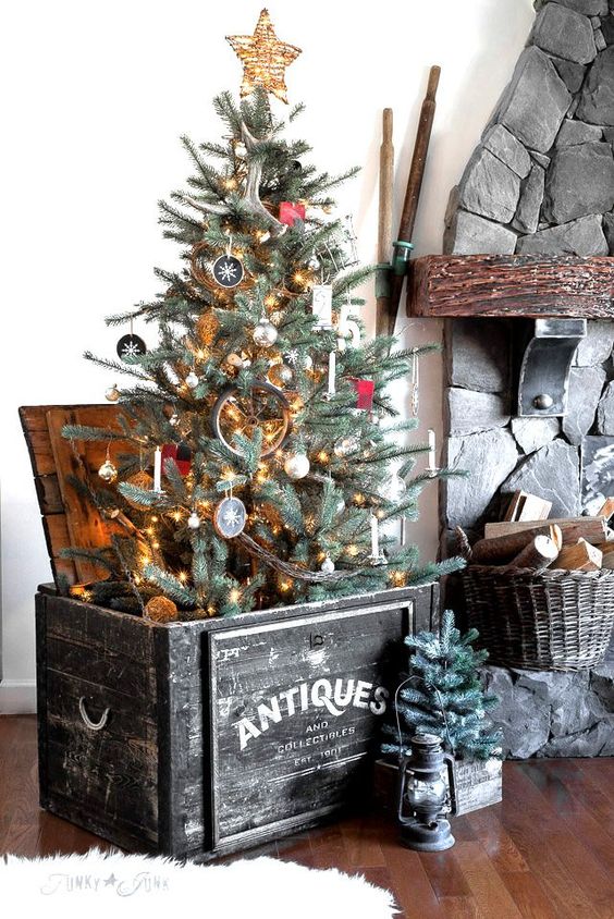 صندوق خشبي أسود به شجرة عيد الميلاد وسلة بها حطب وشجرة صغيرة في قفص لإضفاء طابع ريفي