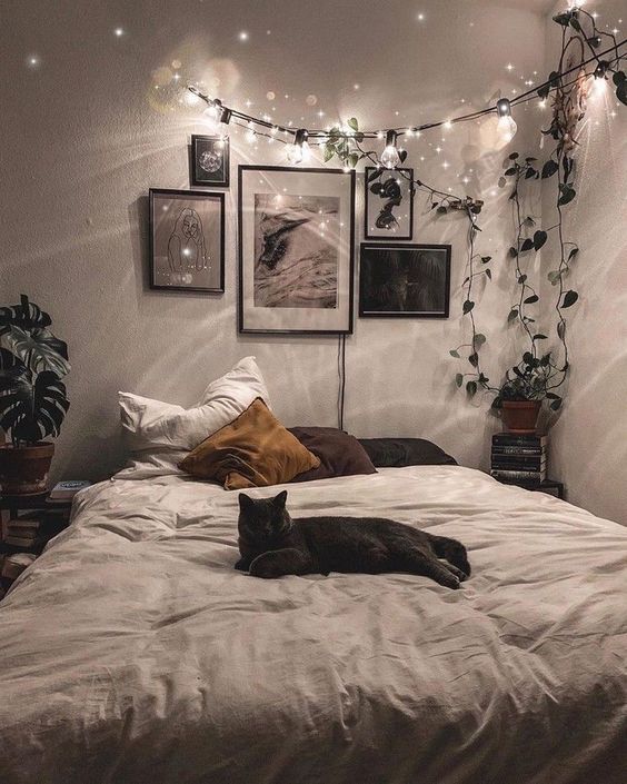 a boho bedroom in neutrals, with a bed, cool pillows, a gallery wall, potted greenery and string lights