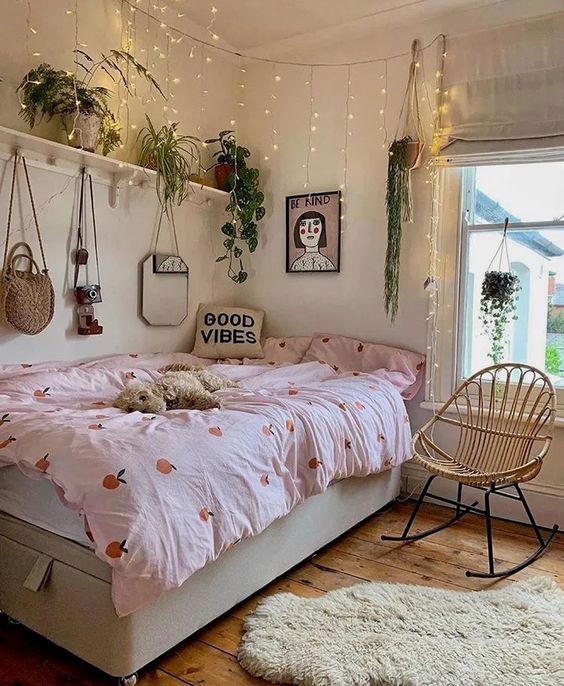 a boho bedroom with a neutral storage bed, pink bedding, a shelf with potted plants, string lights and a rattan chair