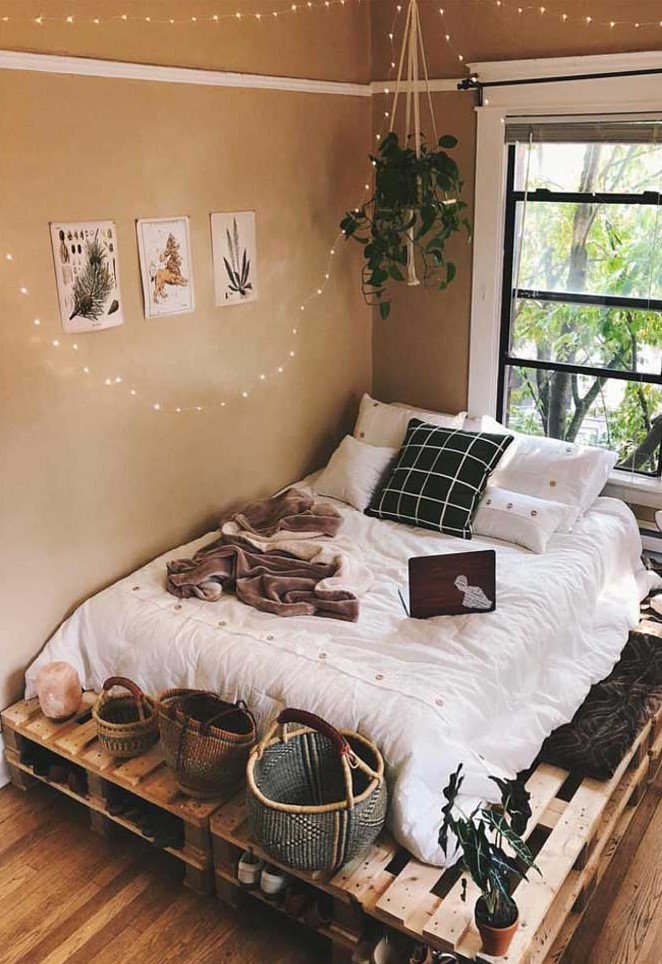 a boho bedroom with tan walls, a pallet bed with black and white bedding, baskets, potted plants and string lights