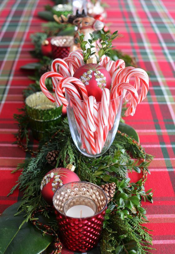 a bold and pretty festive centerpiece of greenery, fir branches, red ornaments, candles and candy canes is very chic