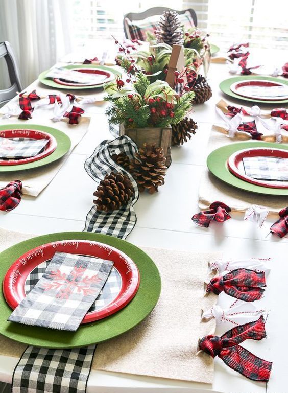 a bold and simple Christmas table with a plaid runner and napkins, large pinecones, faux berries and evergreens and bold plates
