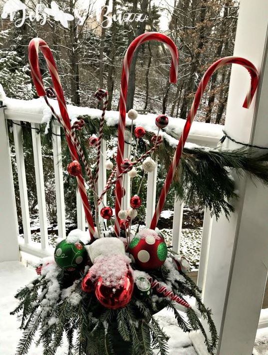 a bold outdoor Christmas decoration of a vase iwth fir branches, bright ornaments and large candy canes is whimsical and bright