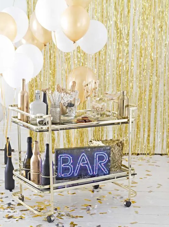 a brass bar cart with white and gold balloons, black and gold bottles and a neon sign